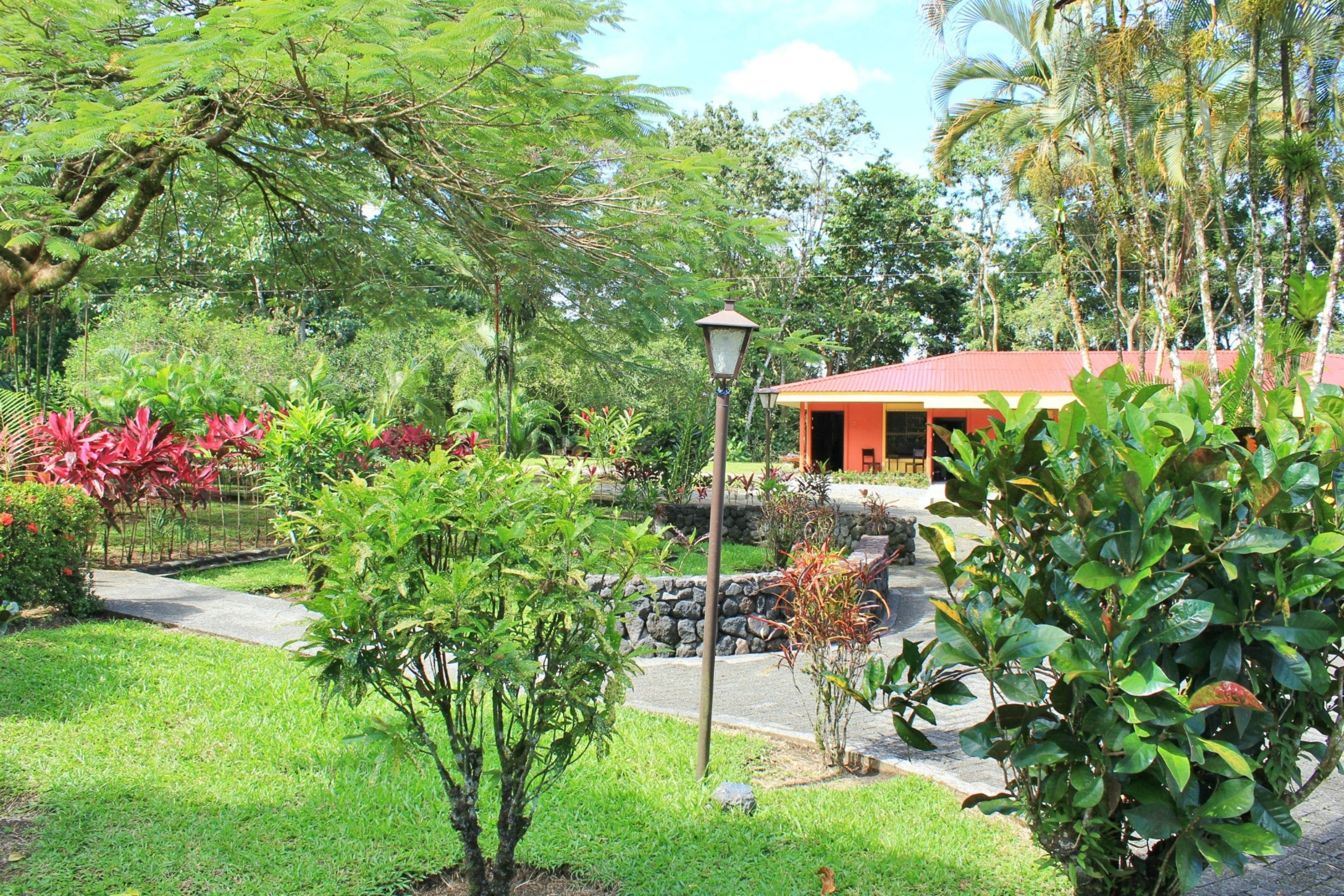 A lush garden with a pathway leading to a building with a red roof.