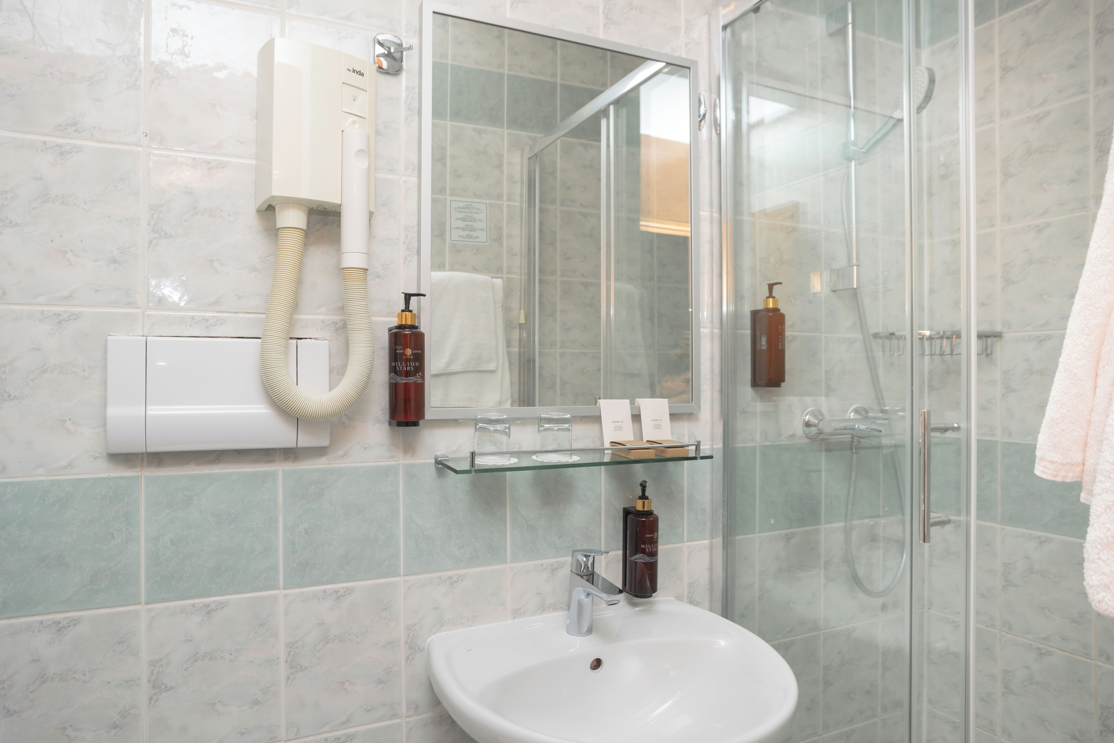 Een badkamer met een douchecabine van glas, een witte wastafel, een glazen plank met toiletartikelen en een spiegel.