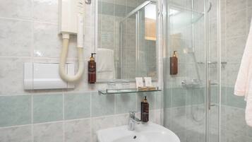 Een badkamer met een douchecabine van glas, een witte wastafel, een glazen plank met toiletartikelen en een spiegel.