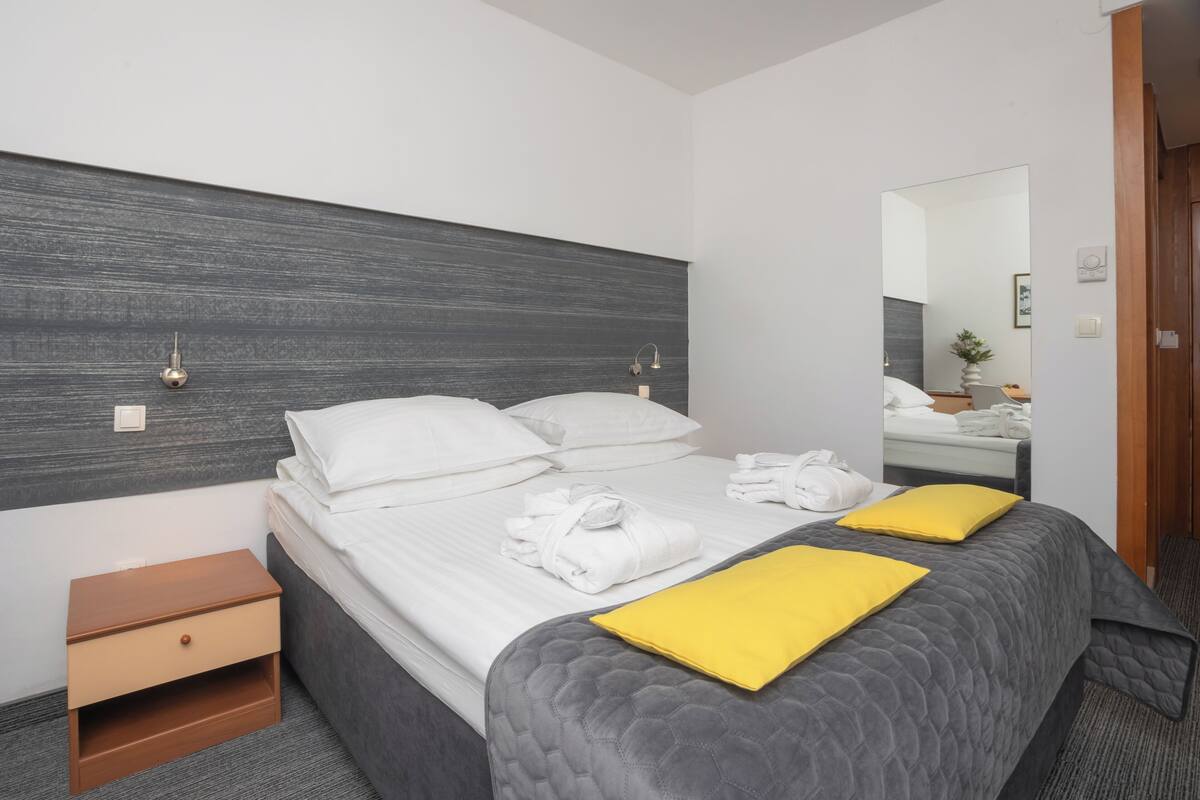 Habitación de hotel con cama, mesita de noche, espejo y baño visible en el reflejo.
