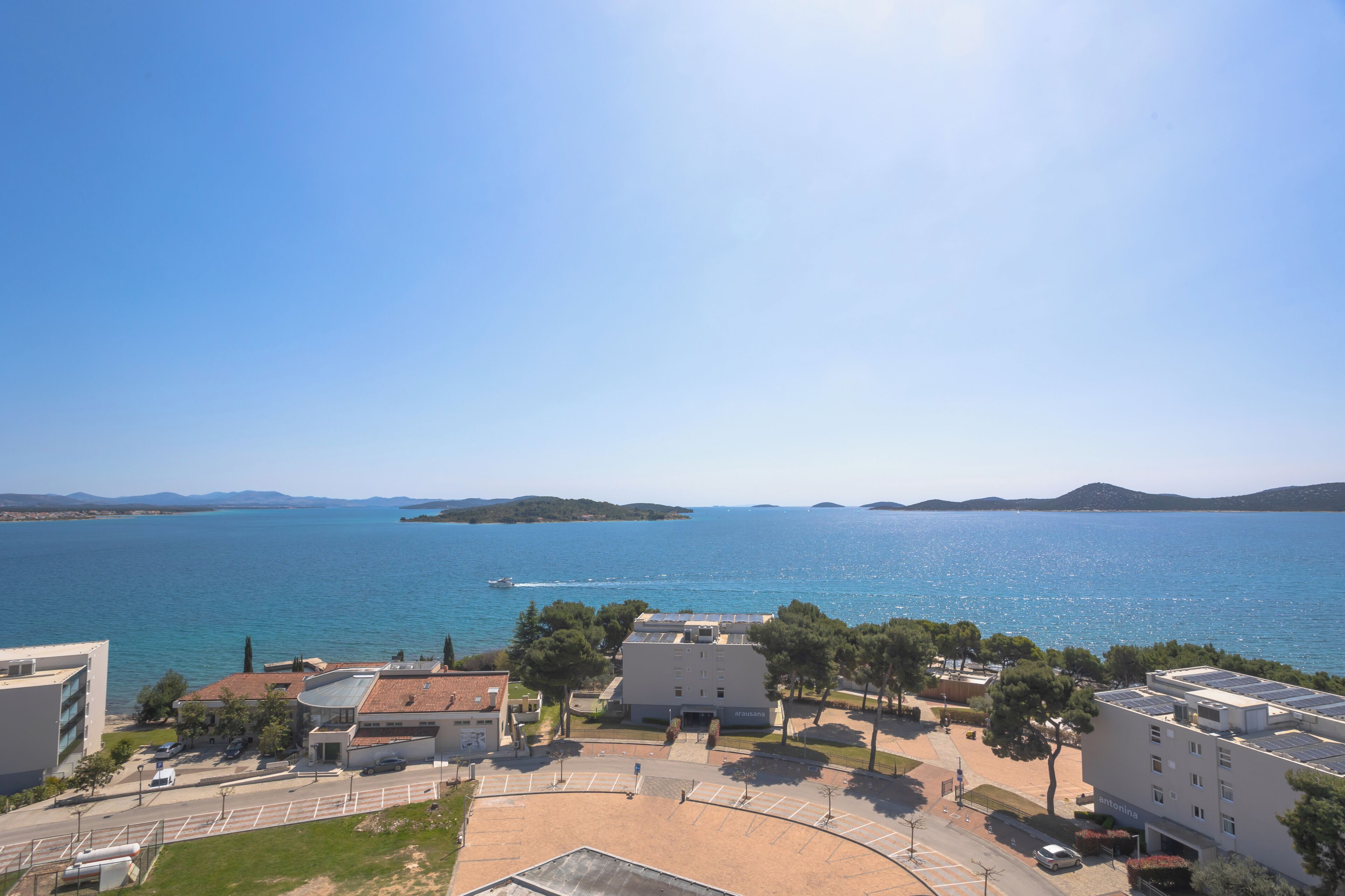 A coastal building complex with a parking area, a road, and a view of the sea.