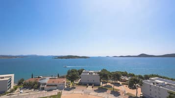 A coastal building complex with a parking area, a road, and a view of the sea.