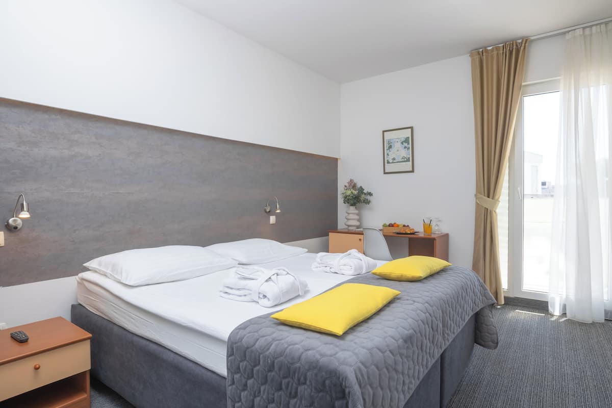 Habitación de hotel con cama, mesitas de noche, lámpara, un cuadro en la pared y ventana con cortinas.