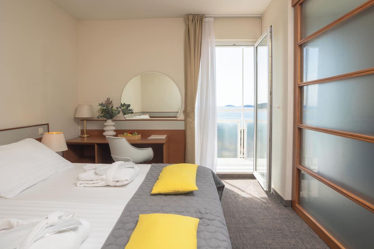 Habitación de hotel con cama, escritorio, silla, espejo y vistas al exterior.