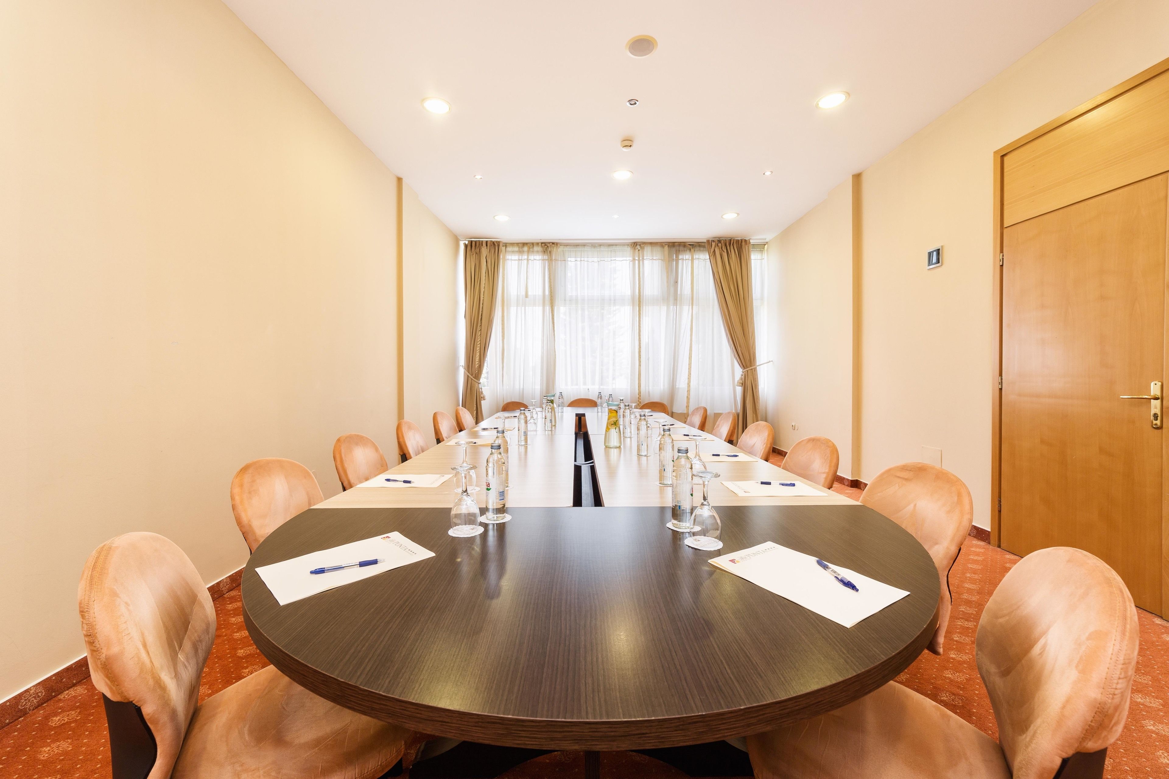 Un salón de conferencias con una mesa larga, sillas y una puerta.