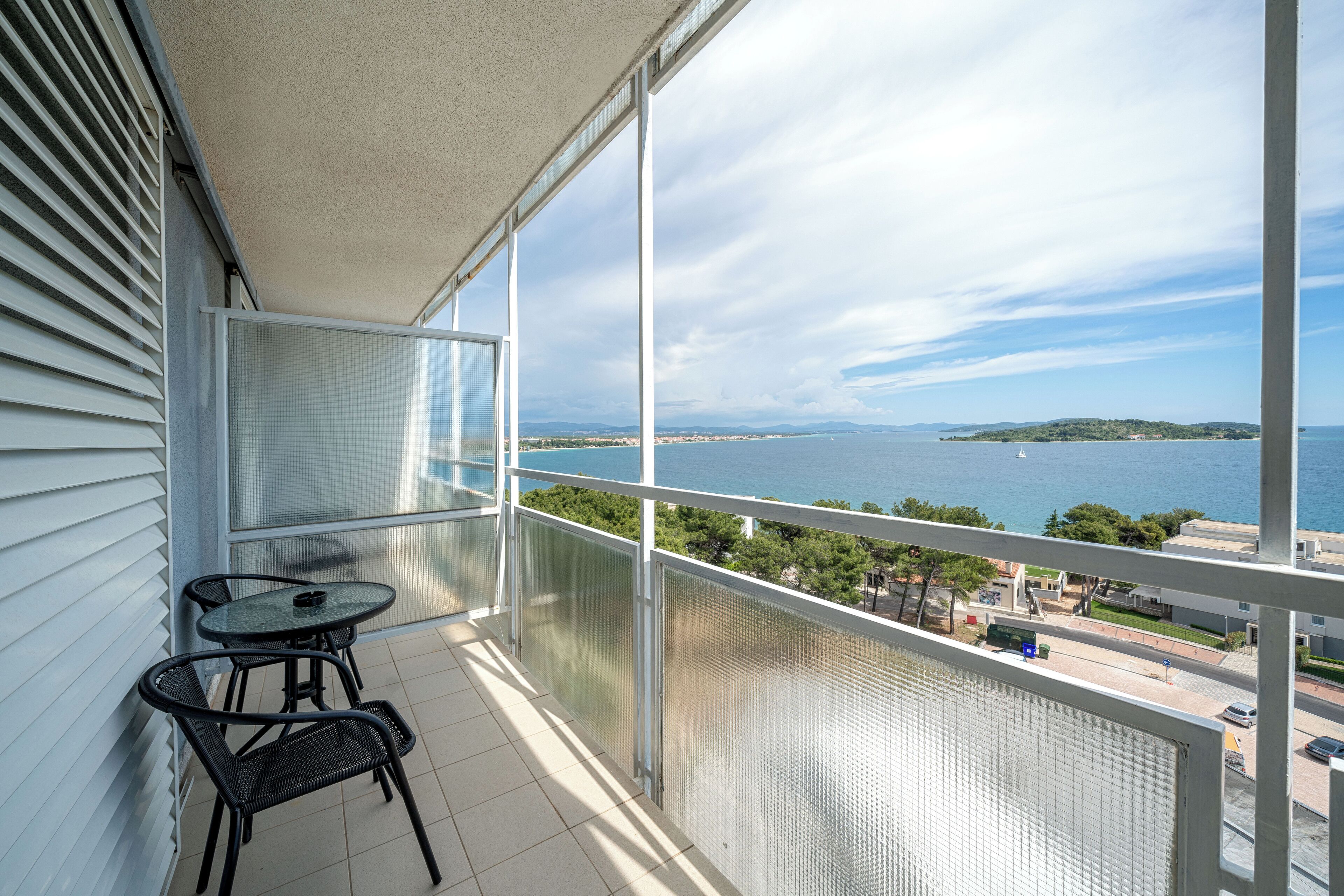 Ein Balkon mit Tisch und Stühlen, der auf ein Gewässer und eine entfernte Insel blickt.