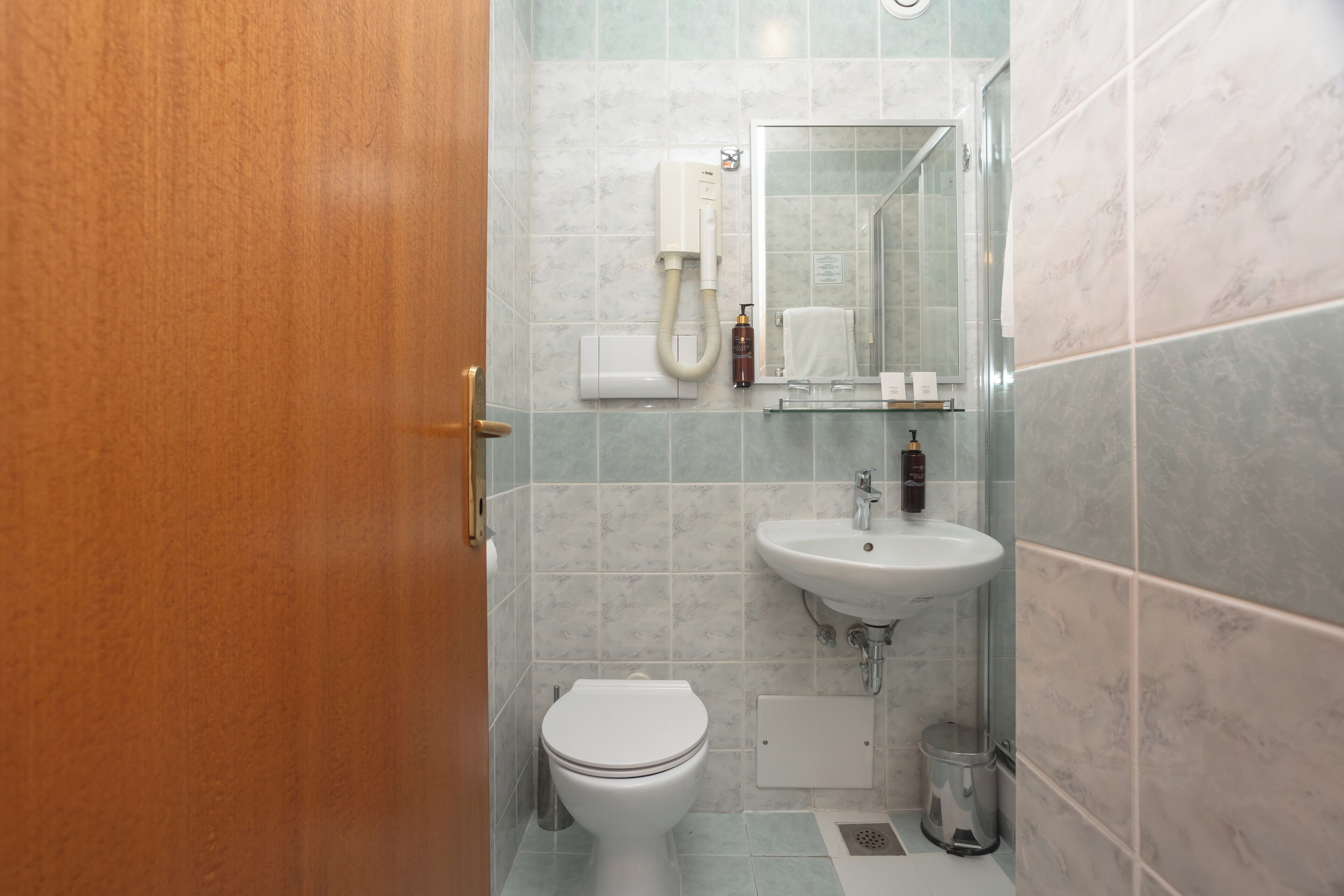 A bathroom with a toilet, sink, mirror, and a hand dryer.