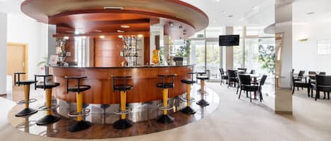 A modern bar area with a central counter, multiple stools, and a seating area with tables and chairs.