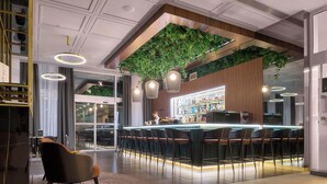 Zona de bar moderna con una pared verde, taburetes y un barman.