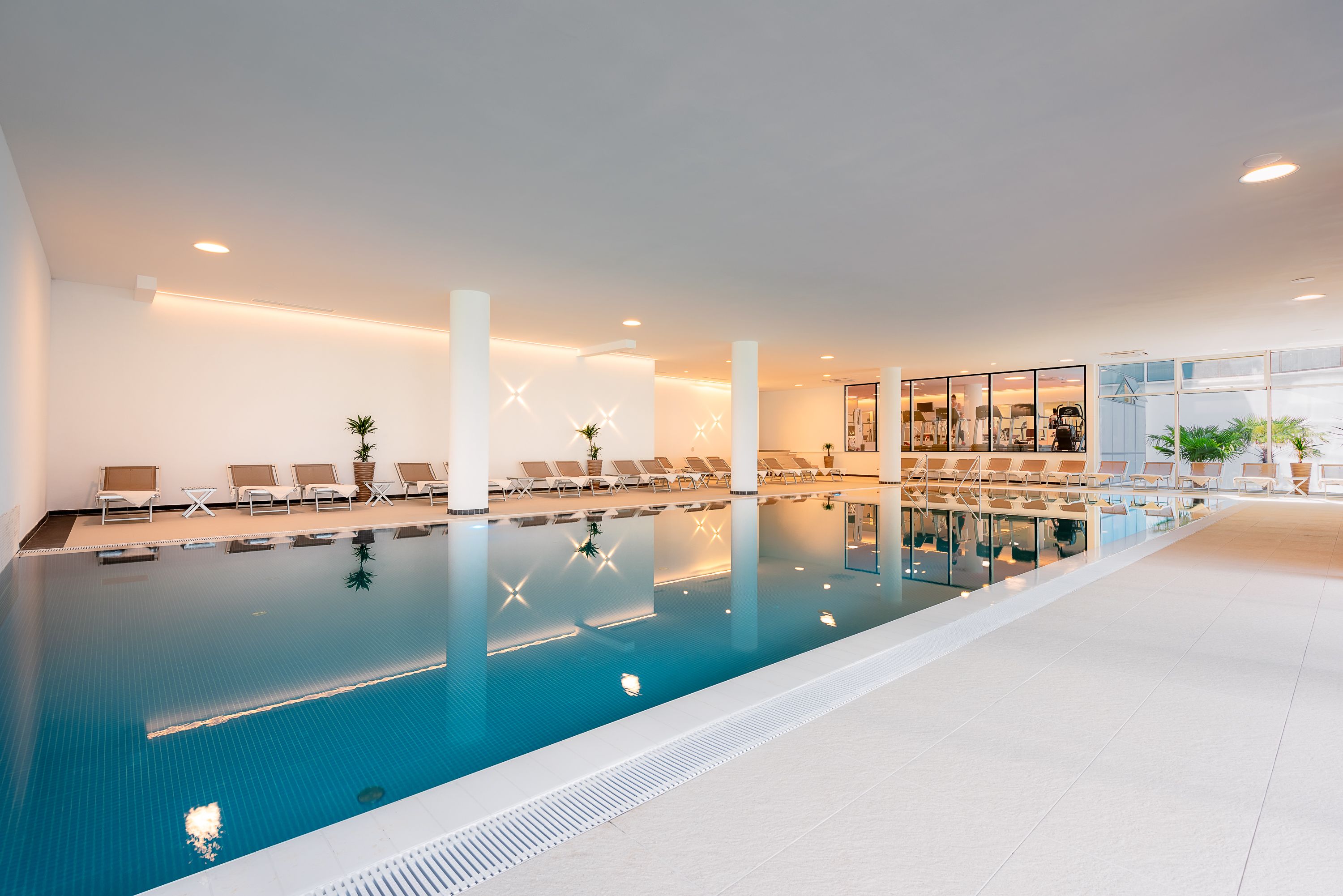 Une piscine intérieure dotée de chaises longues et d’un mur en verre.