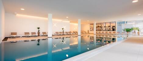 Une piscine intérieure dotée de chaises longues et d’un mur en verre.