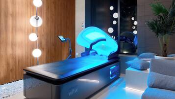 A modern spa area with a massage table, a wooden wall, and a seating area with a plant.