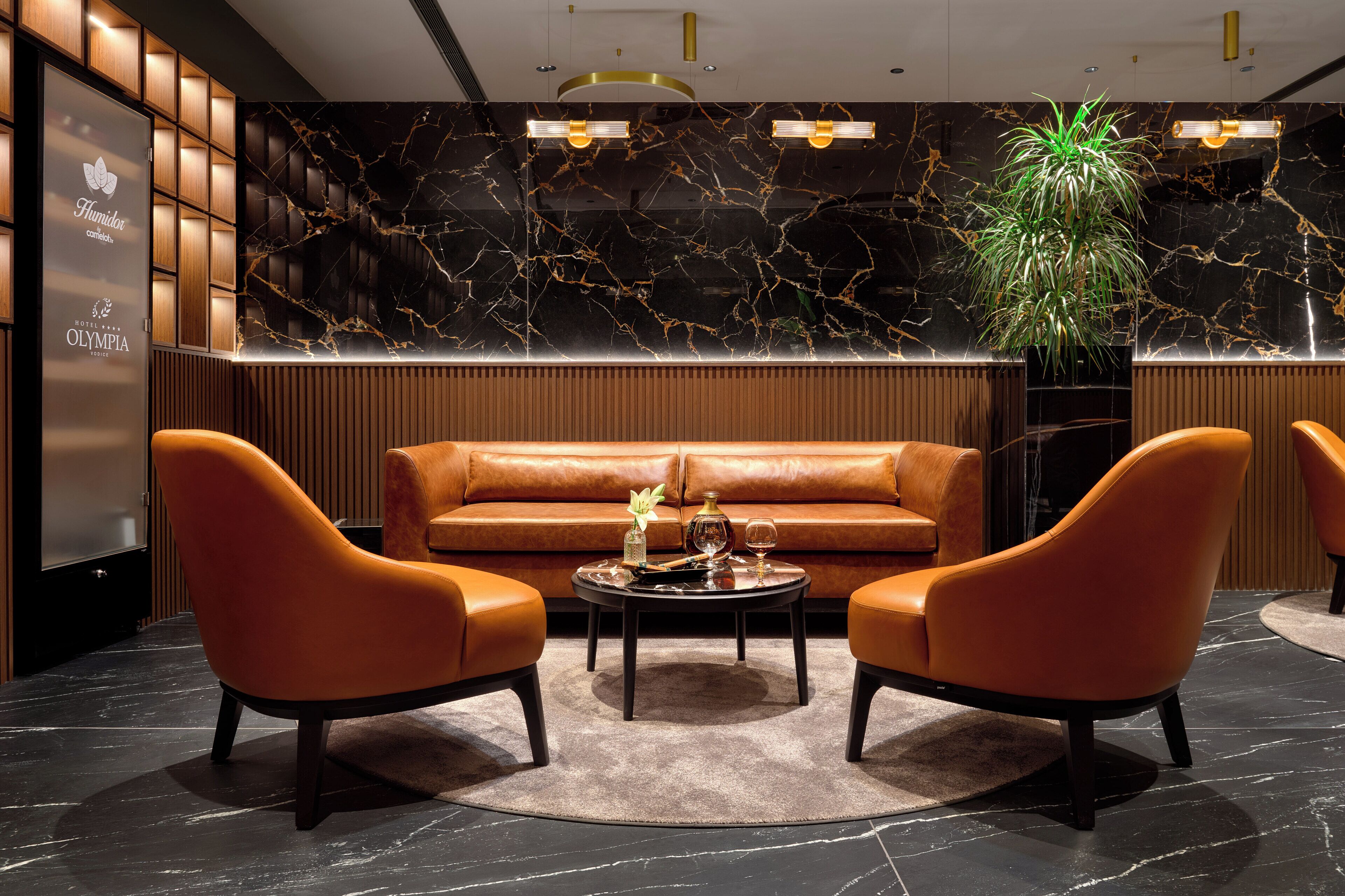 Un lobby moderno con una pared de mármol negro, una pared de paneles de madera, un sofá de cuero y dos sillones de cuero.