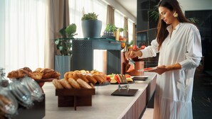 Montaje tipo buffet con pasteles, frutas y una persona sirviendo comida.