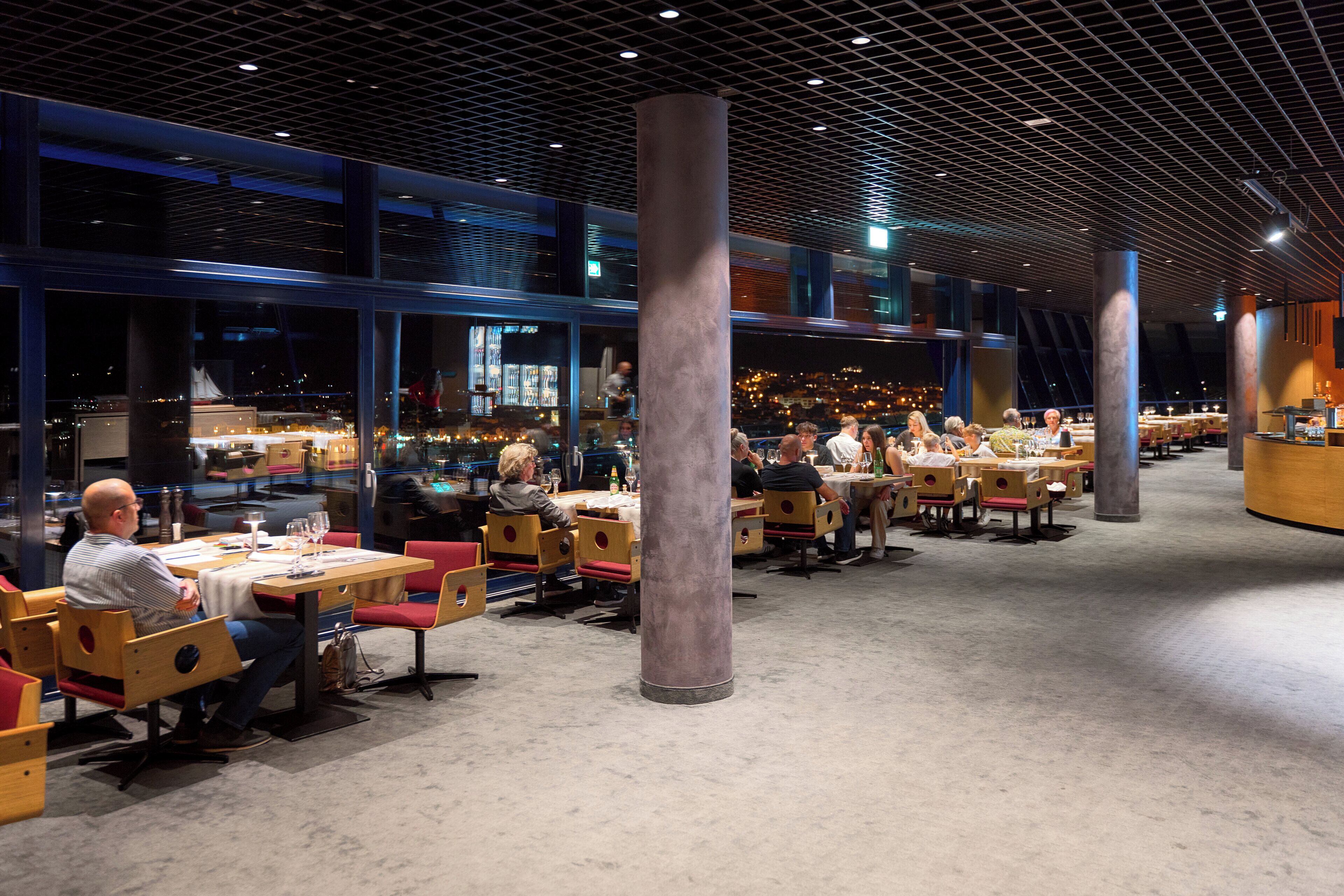 A spacious restaurant with multiple tables and chairs, large pillars, and a modern ceiling design.