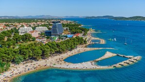 Vista aérea de un pueblo costero con playa, aguas azul cristalino y una mezcla de edificios residenciales y comerciales.