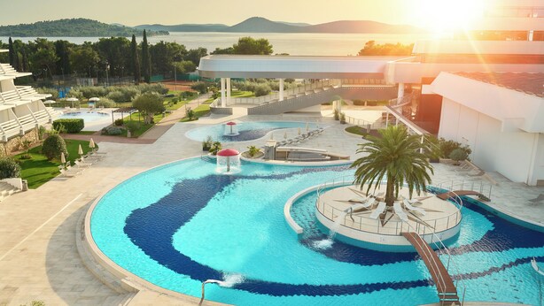 Una piscina de diseño circular en un resort, con una palmera y vista al mar.