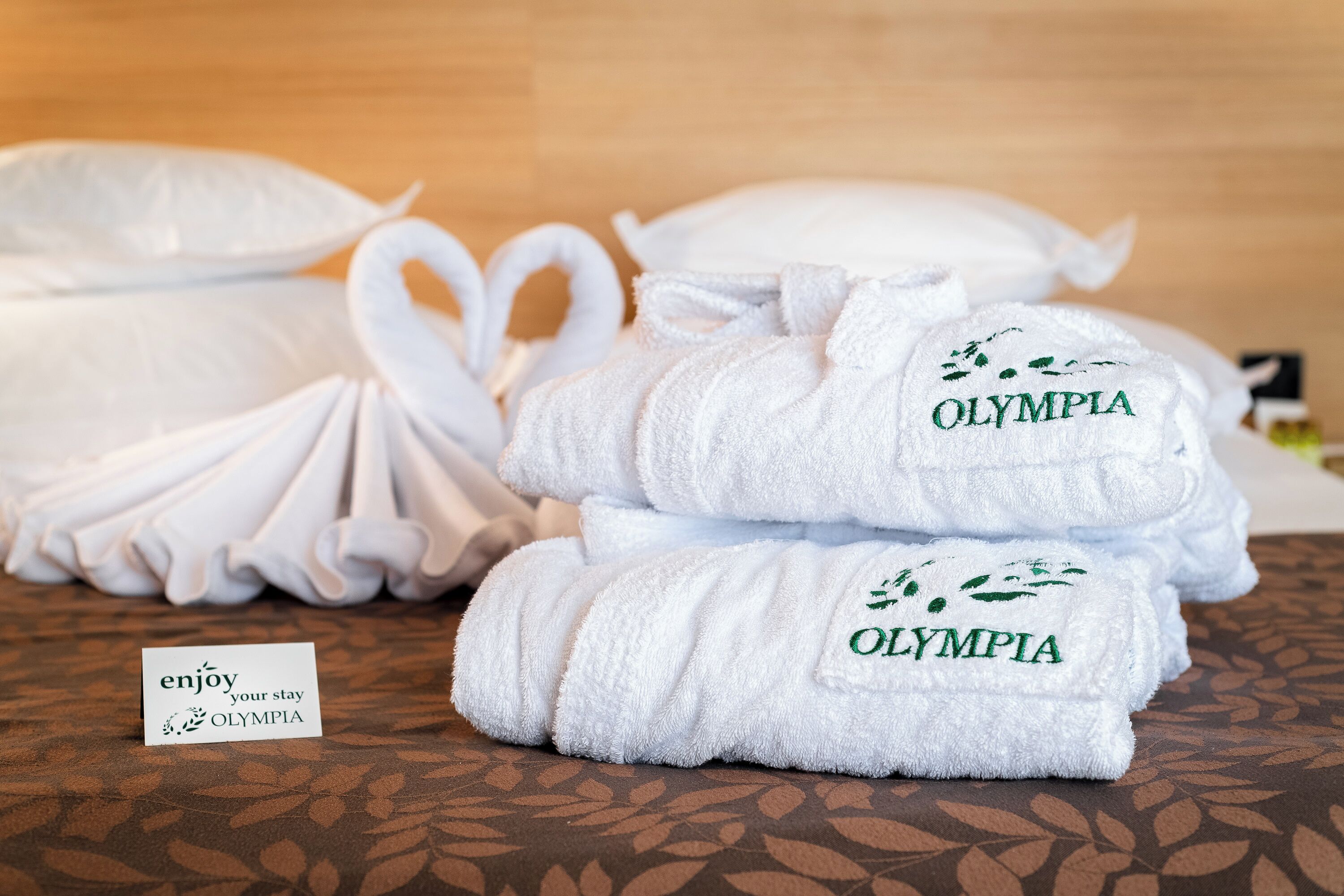 Neatly folded white towels with "OLYMPIA" embroidered on them, placed on a patterned surface.