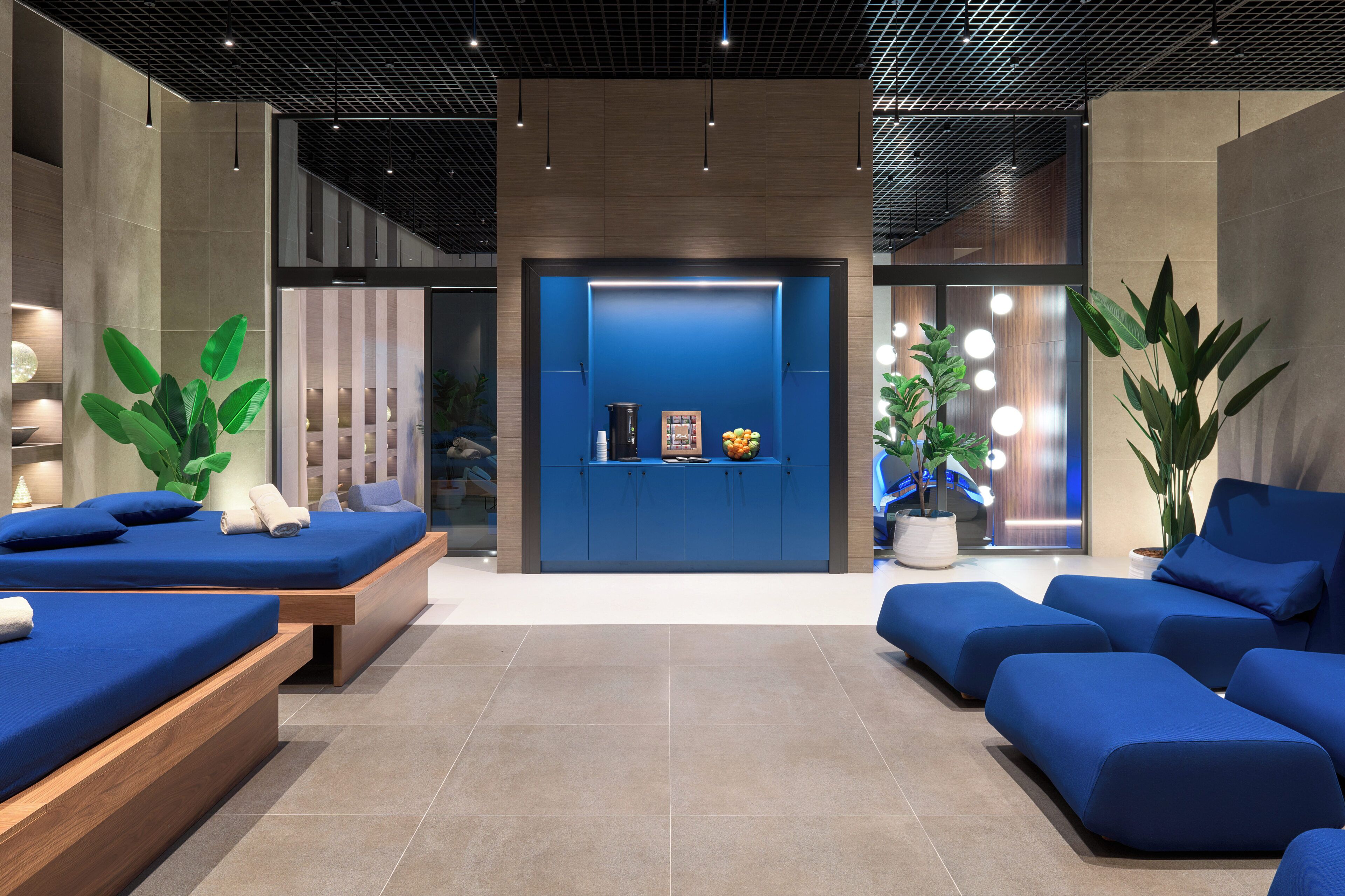 A modern hotel lobby with blue seating areas, a reception desk, and potted plants.