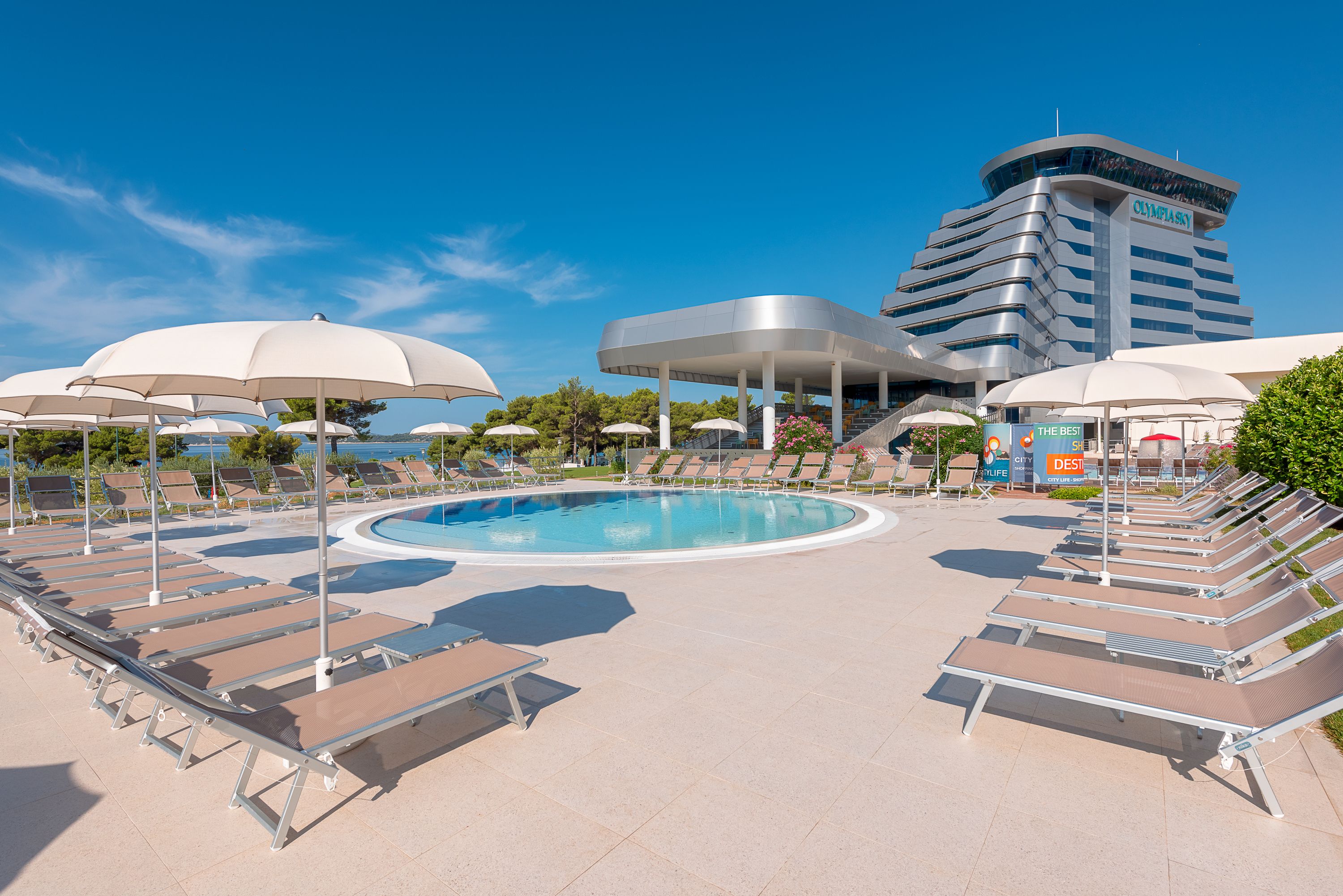 A poolside area with lounge chairs and umbrellas, a swimming pool, and a hotel building in the background.