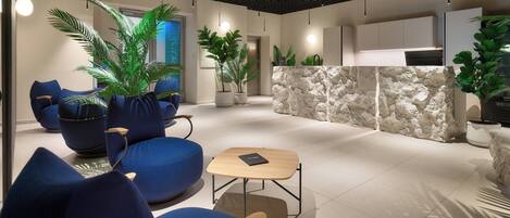 A modern lobby with blue seating, potted plants, and a stone accent wall.