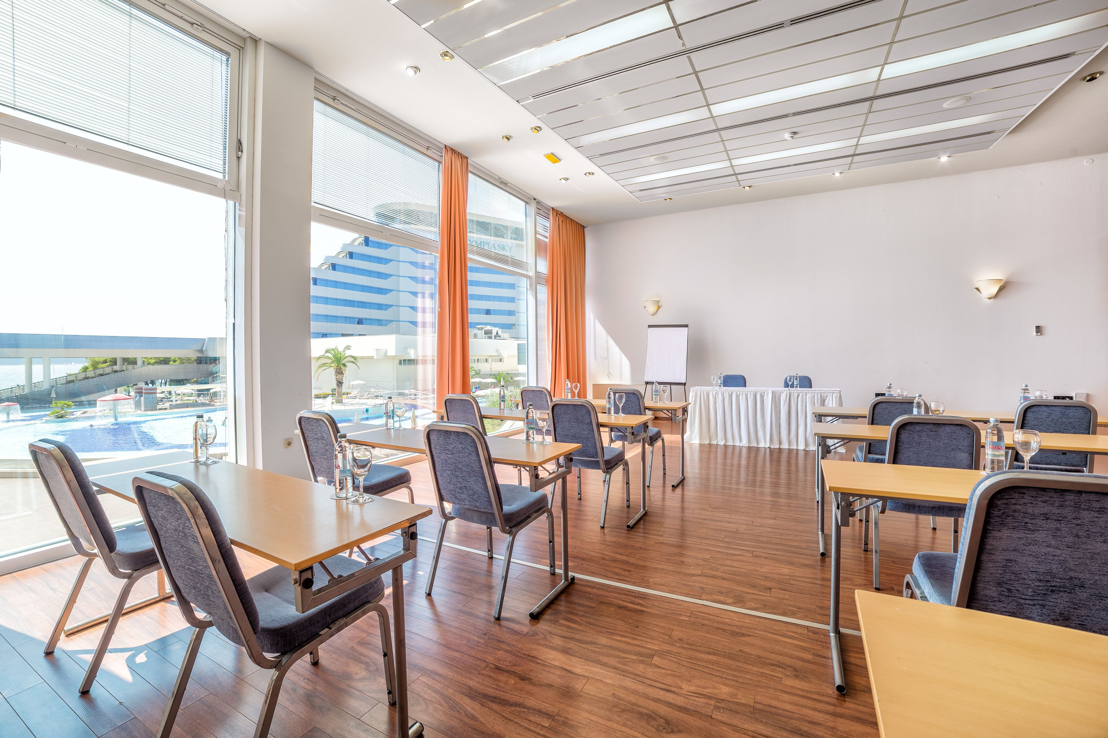 A conference room with tables and chairs, large windows with curtains, and a whiteboard.