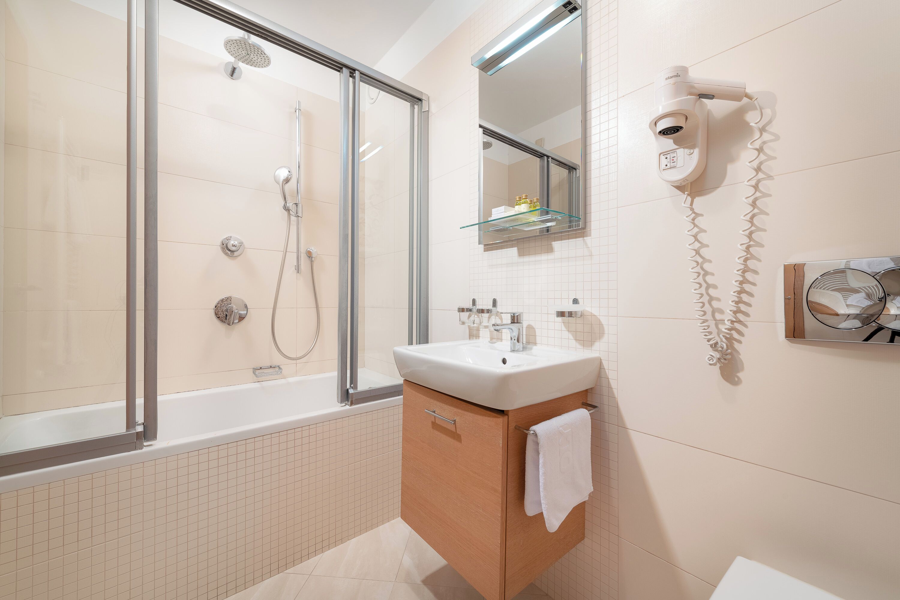 A modern bathroom with a glass-enclosed shower, a white sink, and a hairdryer mounted on the wall.