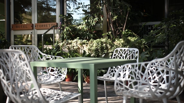 Une table verte avec des chaises blanches est placée devant un bâtiment sur lequel on peut lire les inscriptions « HÔTEL » et « TORRETTA ».