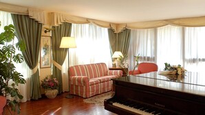 Un salon avec un piano, un canapé à rayures, un fauteuil rouge, une lampe et des rideaux.