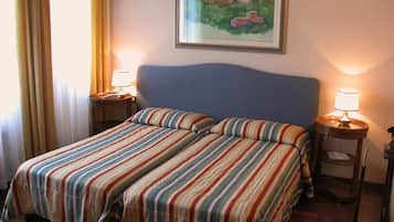 Una cama doble con ropa de cama a rayas, dos lámparas de noche, un cuadro enmarcado en la pared y una ventana con cortinas.