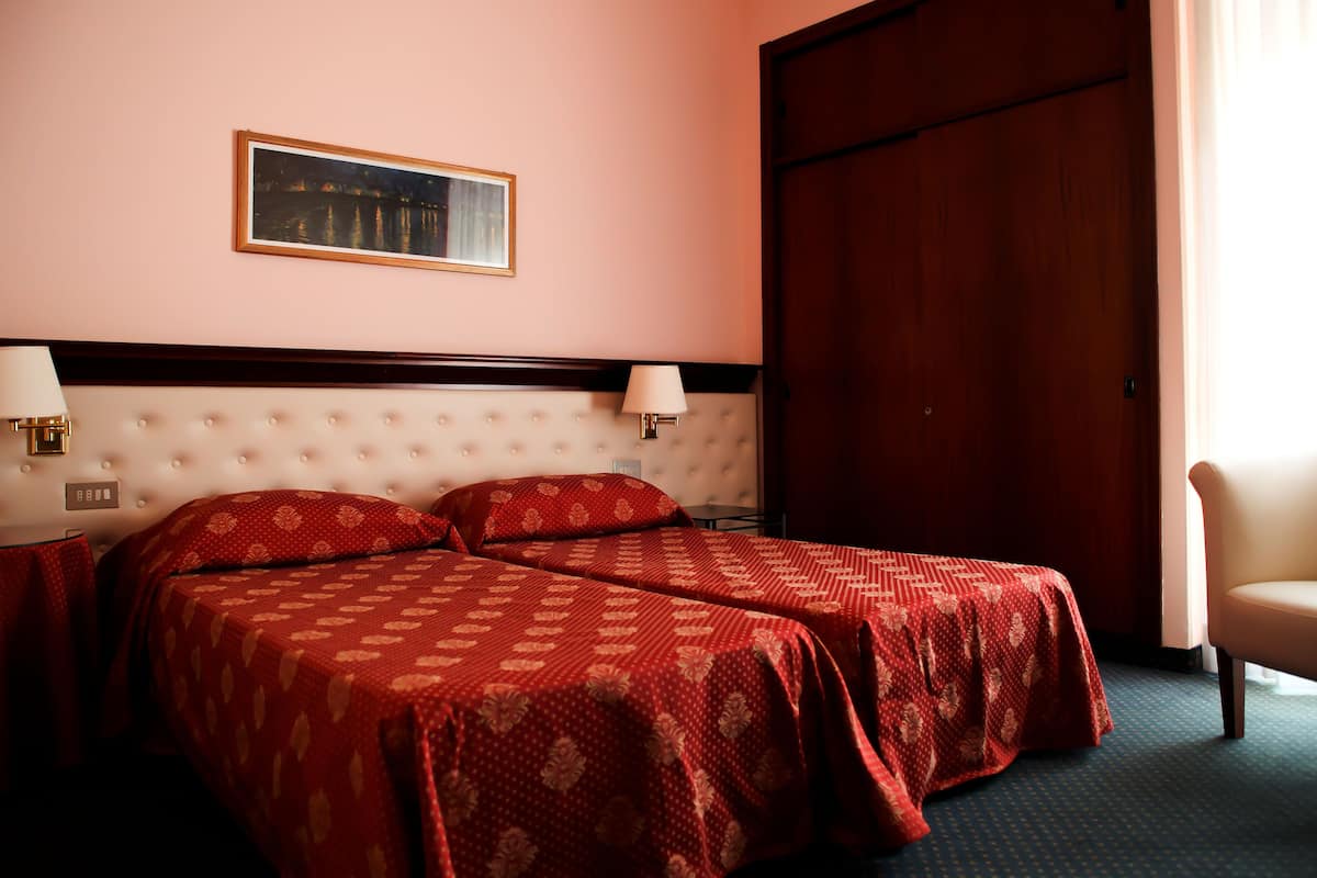 A hotel room with a large bed, two bedside tables with lamps, a wooden door, and a framed picture on the wall.