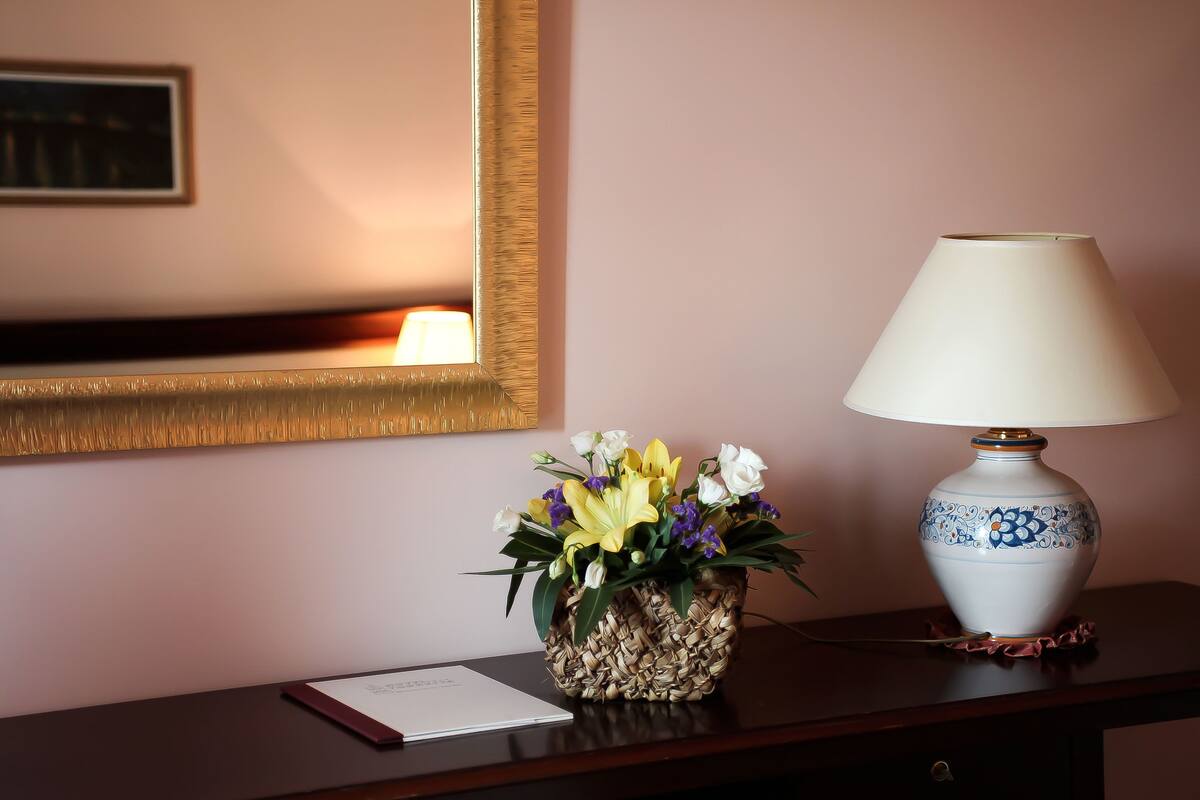 A desk with a lamp, a vase of flowers, and a framed picture on the wall.