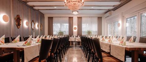Uma sala de jantar formal com mesas grandes, cadeiras e um lustre.