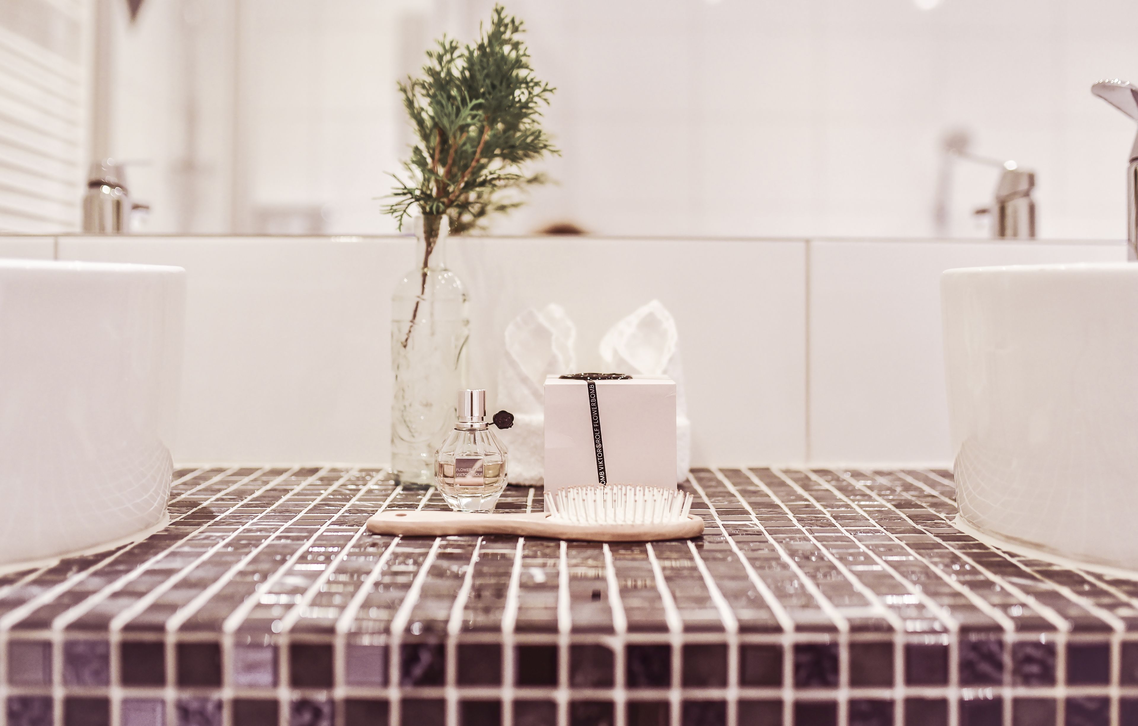 A bathroom with a tiled floor, two sinks, a wooden brush, a glass bottle, and a small plant.