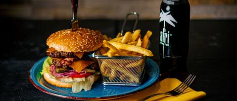 Una hamburguesa acompañada de papas fritas y una botella de Afri Cola sobre un plato azul.