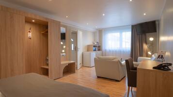 A hotel room with a bed, a seating area with a table, a small kitchenette, and a TV.