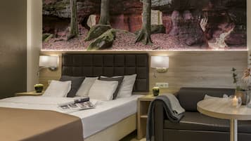 Una habitación de hotel moderna con una cama grande, un sofá, una mesita y un mural en la pared con un paisaje forestal.