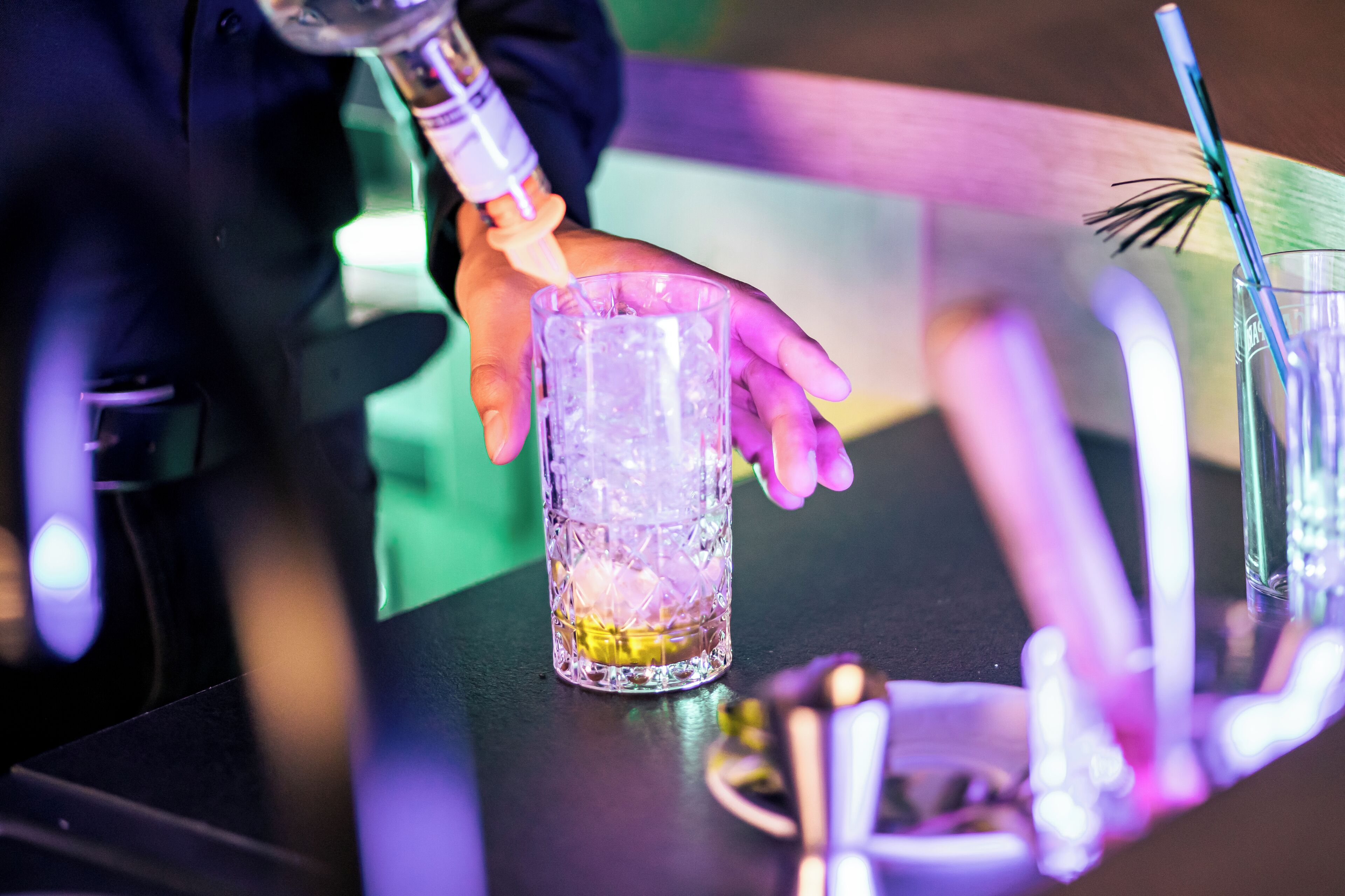 A bartender pouring a drink into a glass with ice.