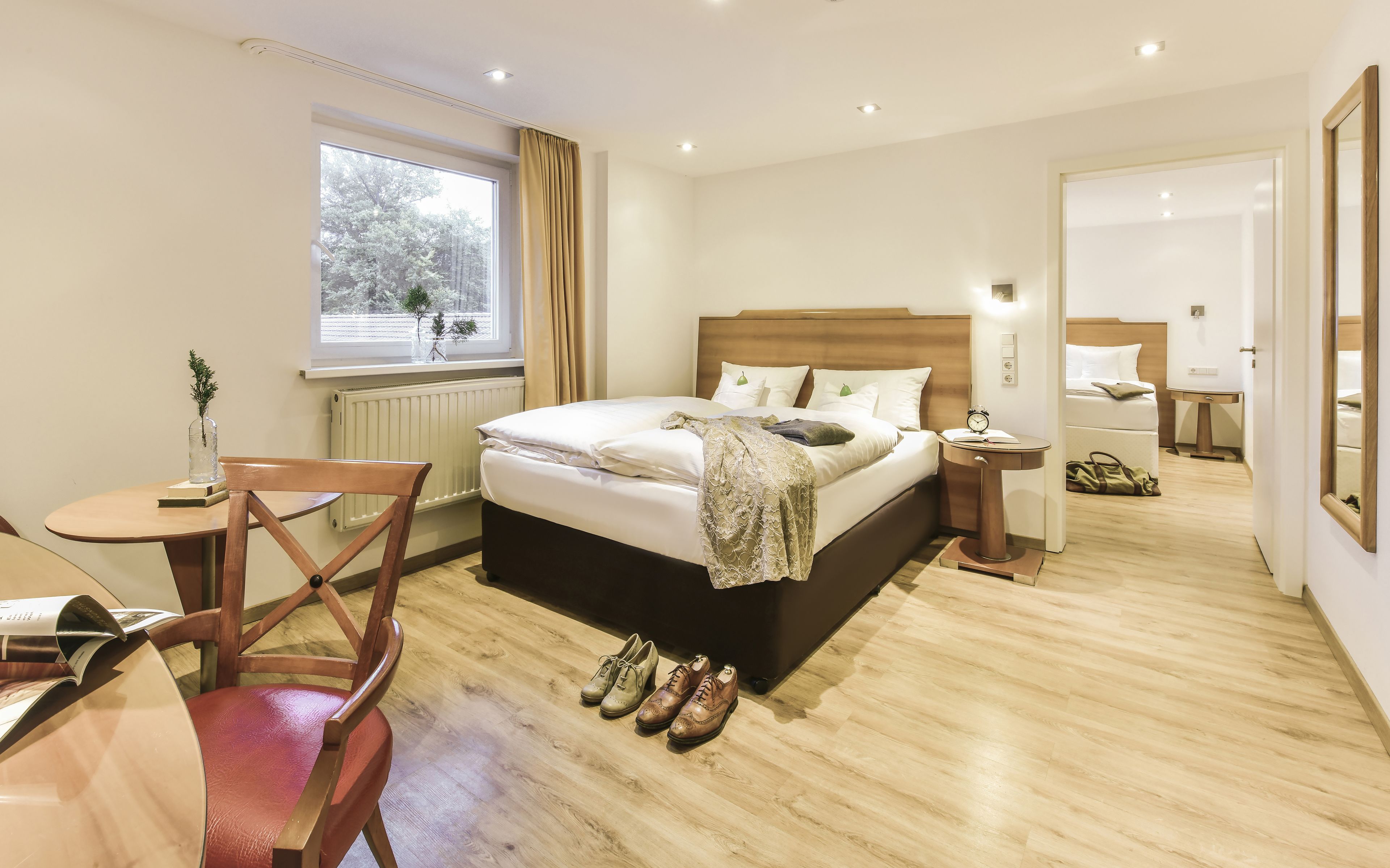 A hotel room with a bed, bedside table, chair, and a window with a view of trees.