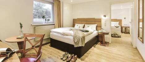 A hotel room with a bed, bedside table, chair, and a window with a view of trees.