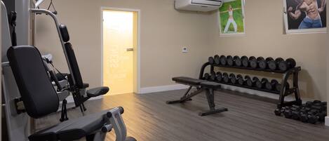 A gym with exercise equipment, a bench, and a rack of dumbbells.