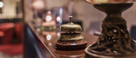 A close-up of a brass lamp with a glass shade and a wooden jar with a lid on a reflective surface.