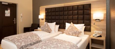 A hotel room with a double bed, two bedside tables, a headboard, and a wall-mounted lamp.