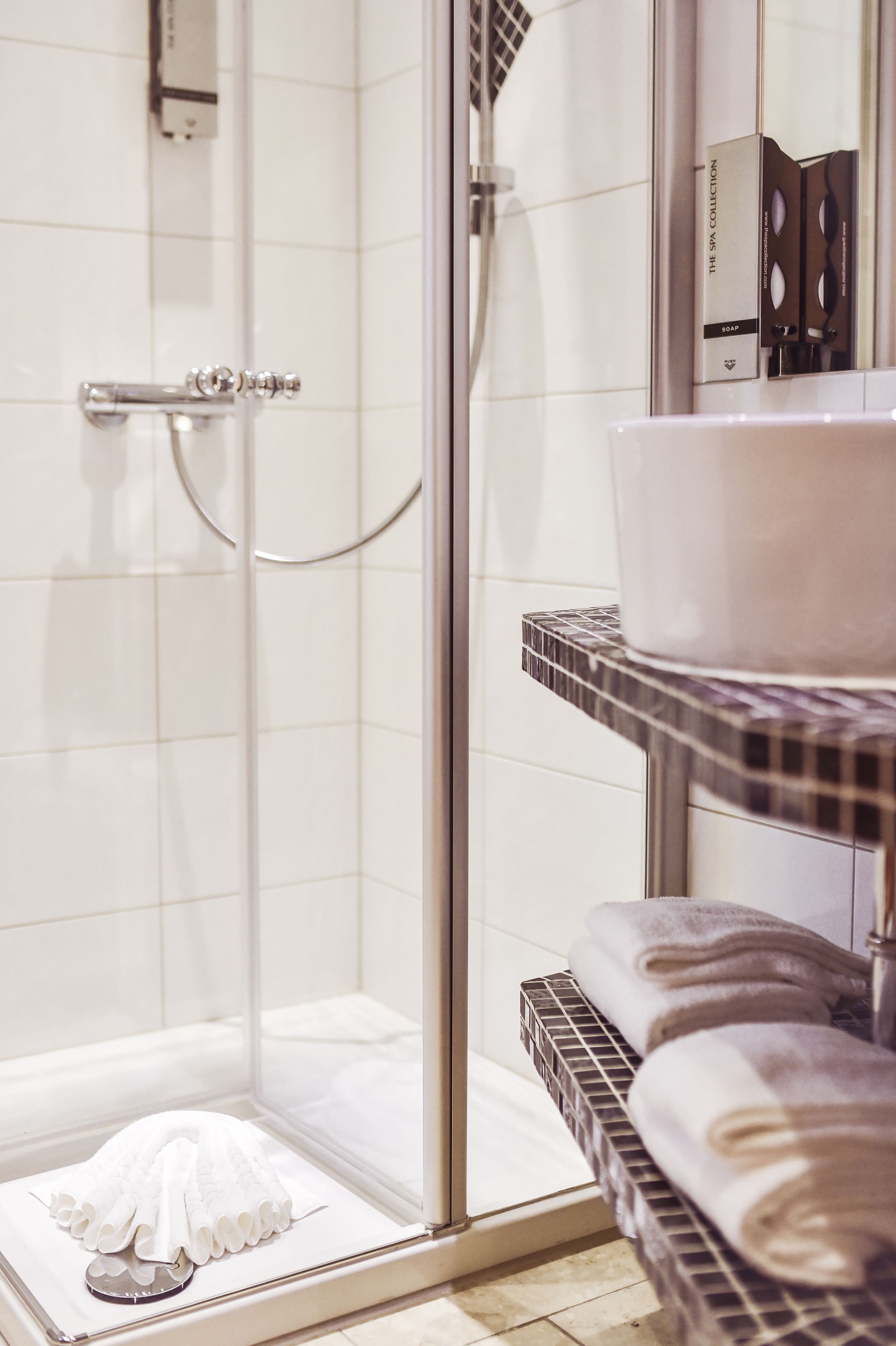 Un bagno moderno con box doccia in vetro, lavandino bianco e asciugamani piegati ordinatamente su uno scaffale.