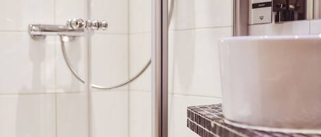 Un bagno moderno con box doccia in vetro, lavandino bianco e asciugamani piegati ordinatamente su uno scaffale.