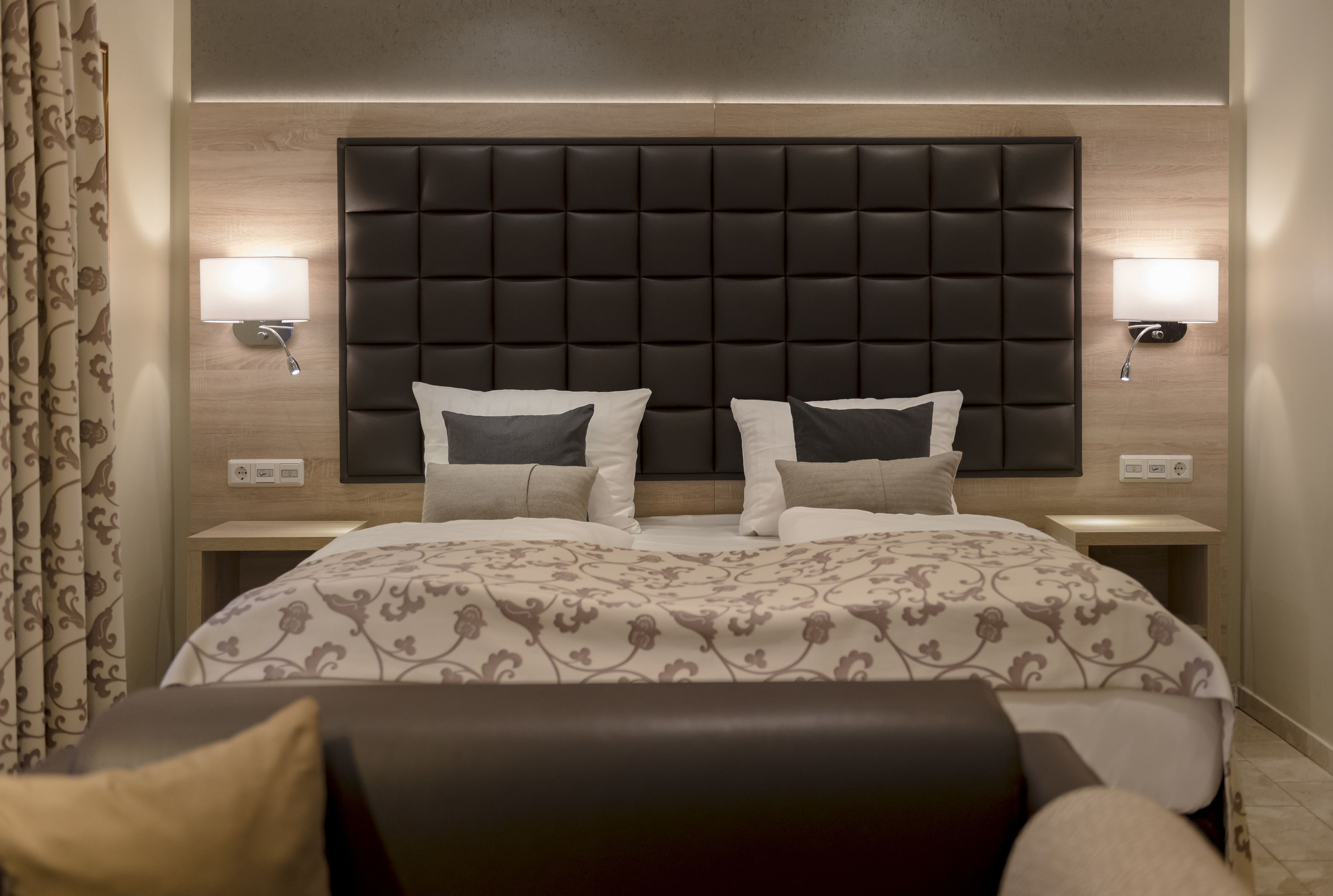 Ein Hotelzimmer mit einem großen Bett, zwei Nachttischen, einer modernen Kopfteil und Wandleuchten.