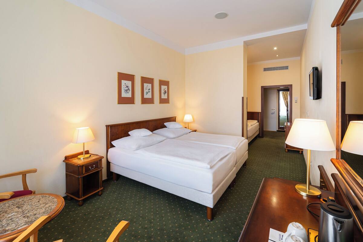 Una habitación de hotel con una cama, dos lámparas de noche, un escritorio con lámpara, una silla y una mesita.