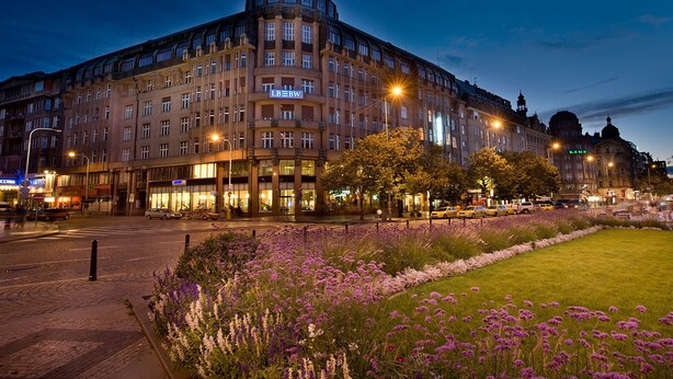 A large, historic building with multiple floors and a prominent corner entrance, surrounded by a well-maintained garden with purple flowers. - EA Hotel Rokoko (Prague)