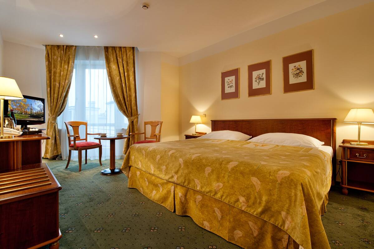 Una habitación de hotel con una cama grande, un escritorio con una computadora, una silla y dos mesitas de noche con lámparas.