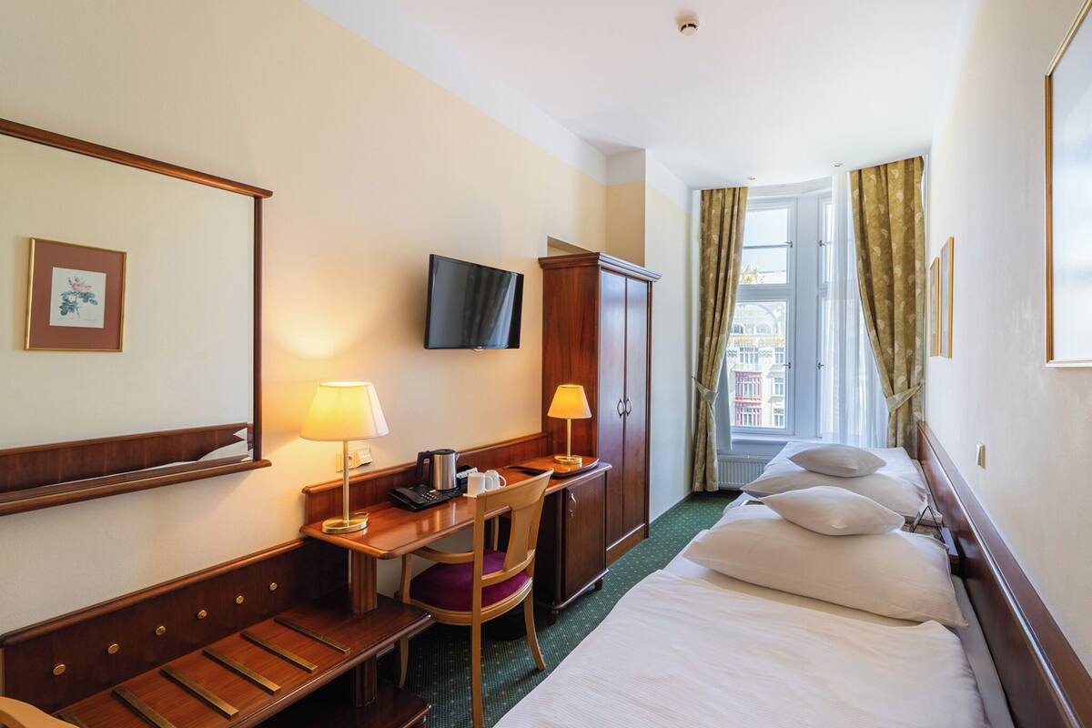 Habitación de hotel con cama, escritorio, silla, televisor y vistas a edificios por la ventana.